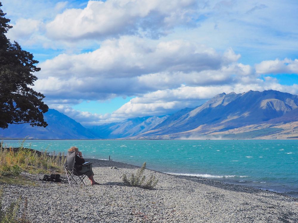Nicky sitting in a camping chair on Lake Ohau's pebble beach