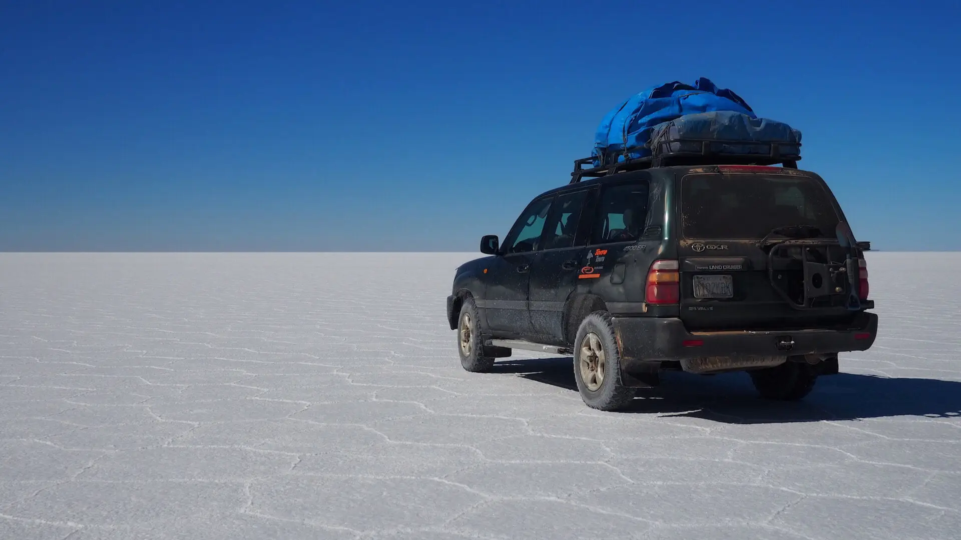 A car with a full laden roof rack is parked on a flat white landscape made of salt