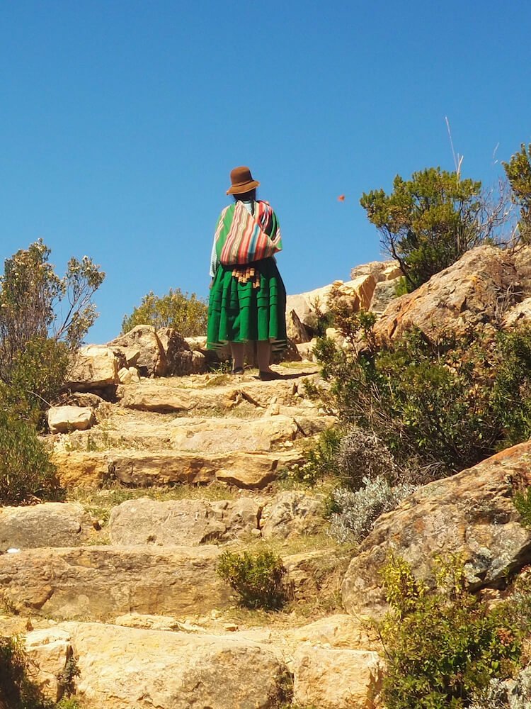 A cholita in traditional dress climbing to Cerro Queñuani