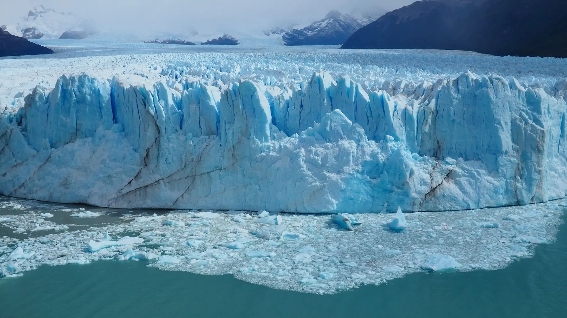 A lake with icebergs in the foreground and a large mass of ice behind it stretching out into the background
