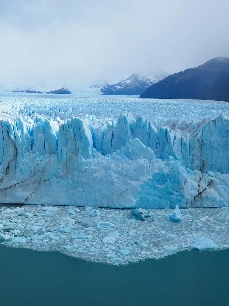 A lake with icebergs in the foreground and a large mass of ice behind it stretching out into the background