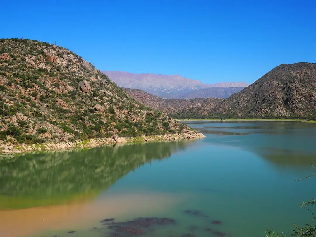 A blue lake surrounding green and sand coloured hills