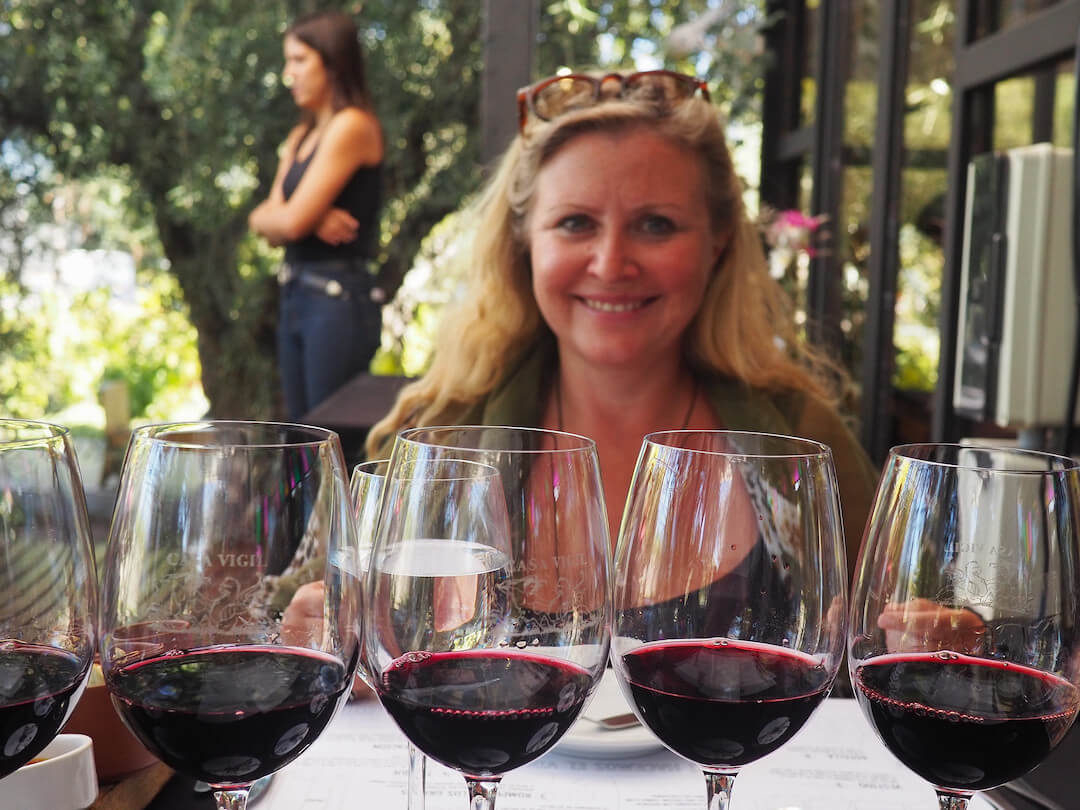 Tasting glasses of red wine in the foreground and a smiling woman in the background