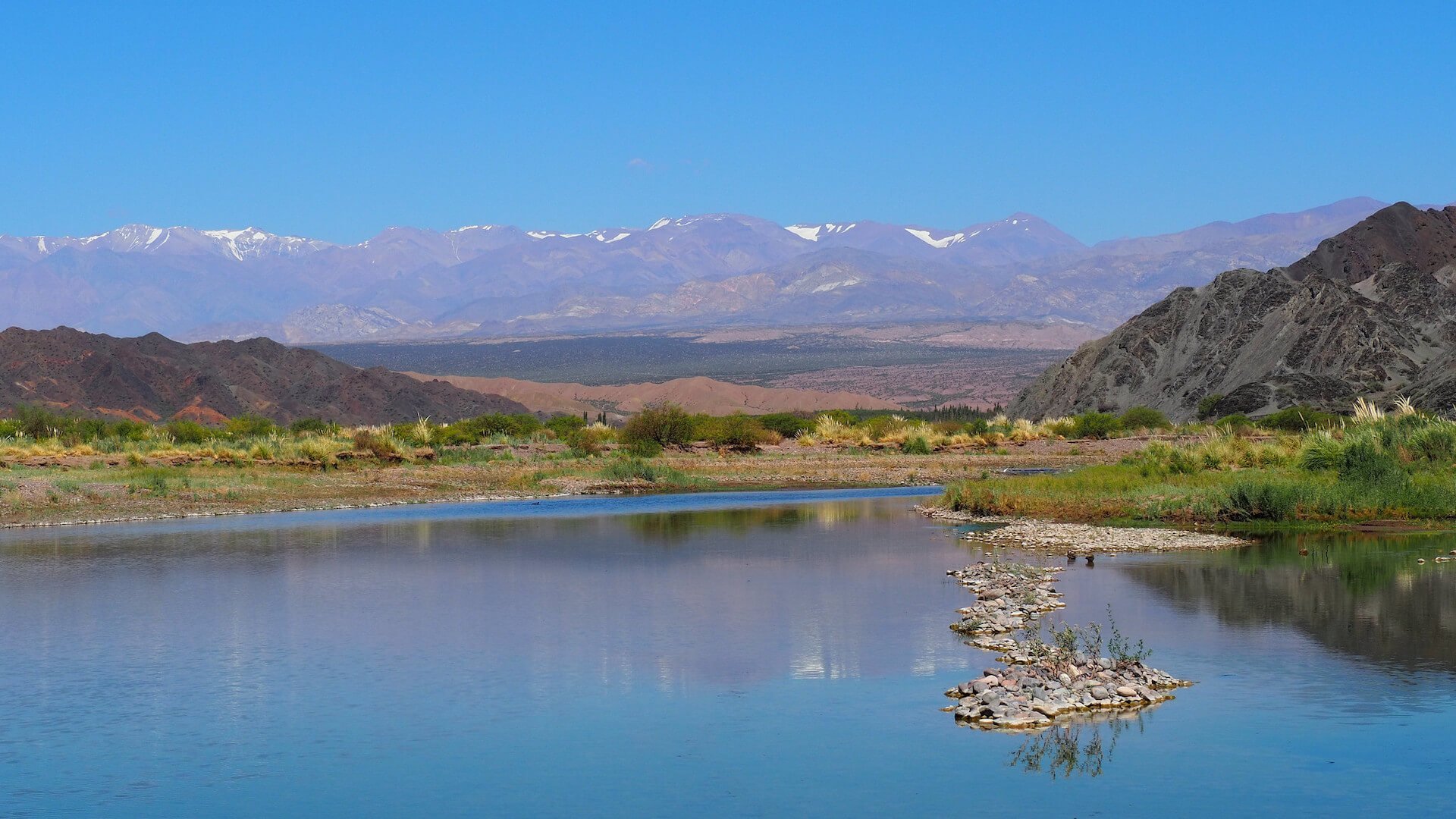 A blue lake with an island of stones and mountains in the background