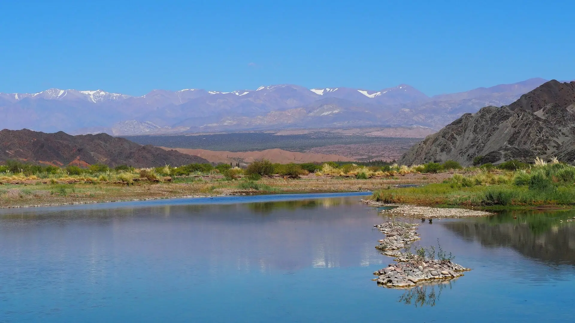 A blue lake with an island of stones and mountains in the background