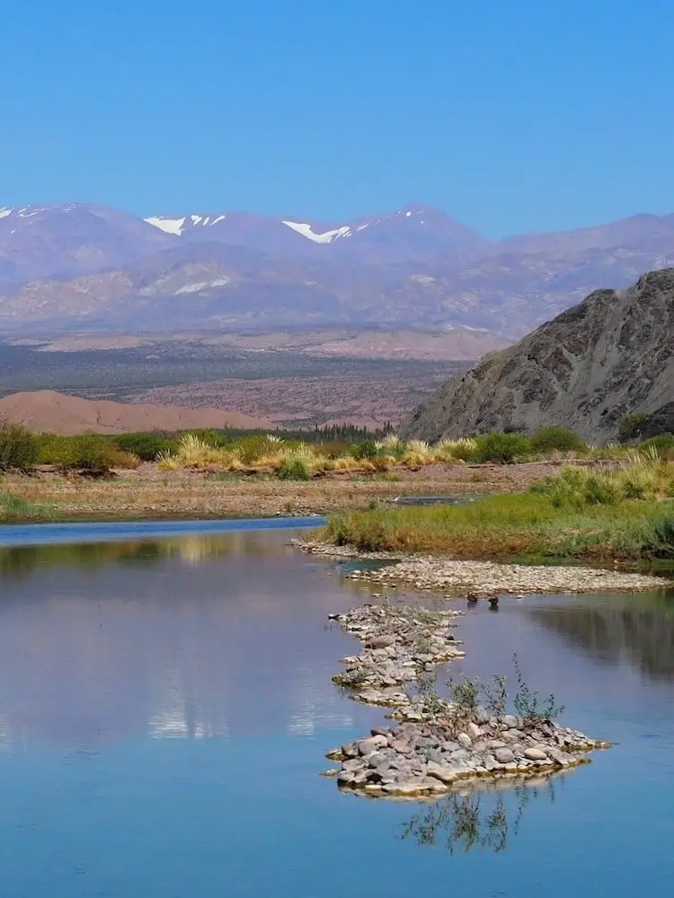 A blue lake with an island of stones and mountains in the background
