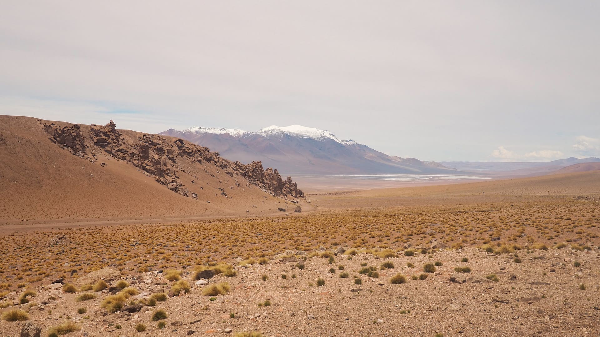 A desert road with lake and snow-capped mountains in the background