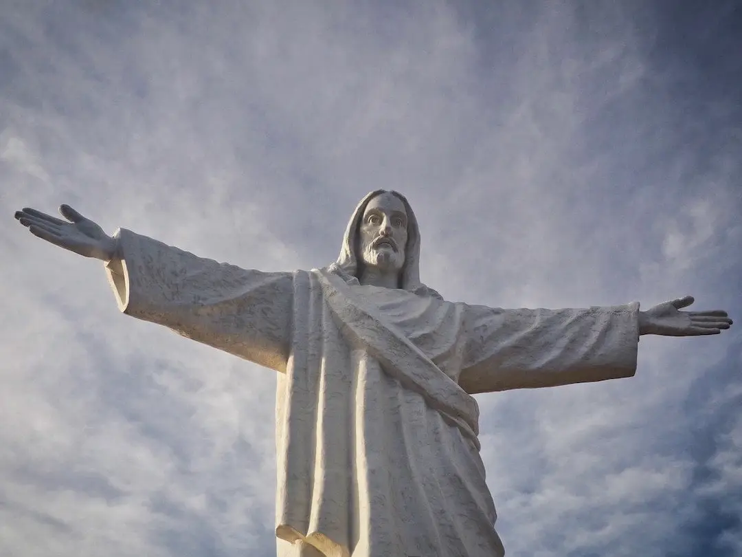 A white statue of a man with outstretched arms against a blue sky with white clouds