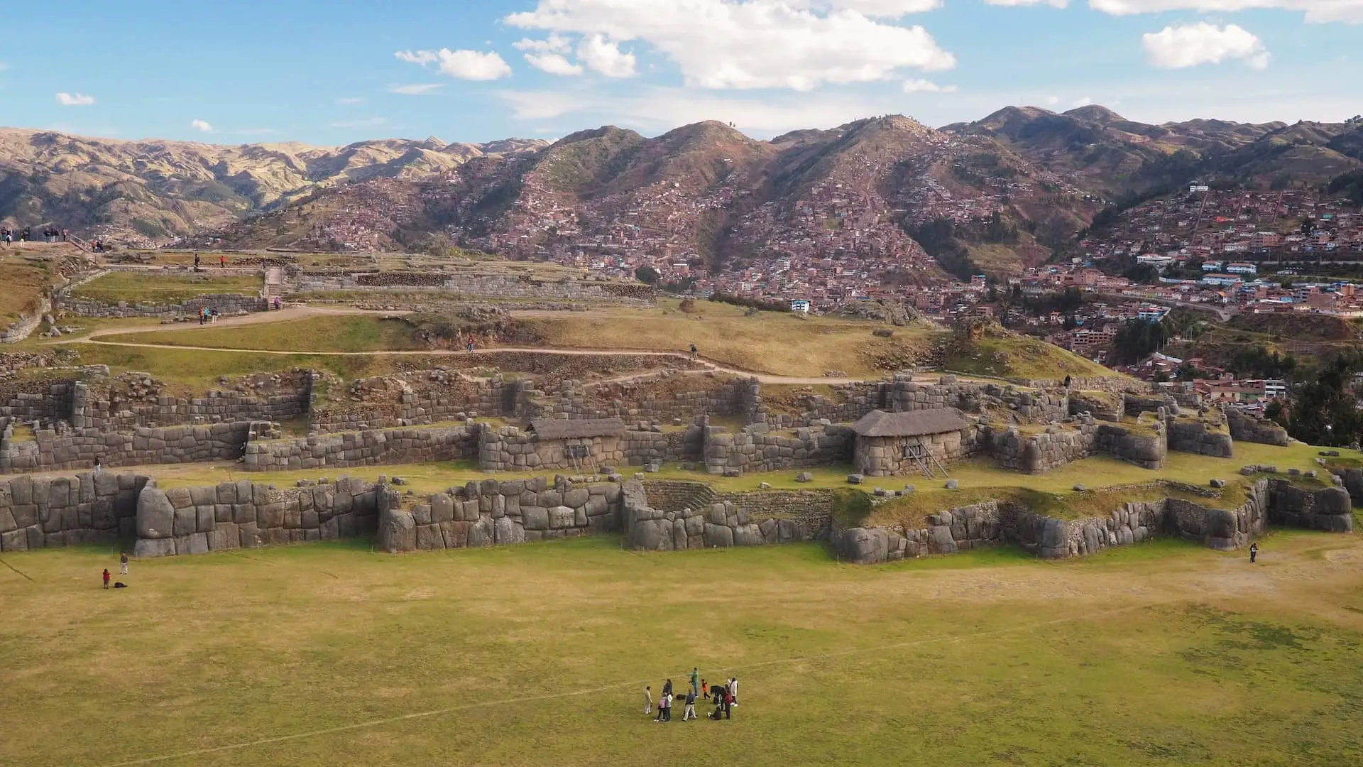 A panoramic view of ruined stone walls with red roofed houses and mountains in the background