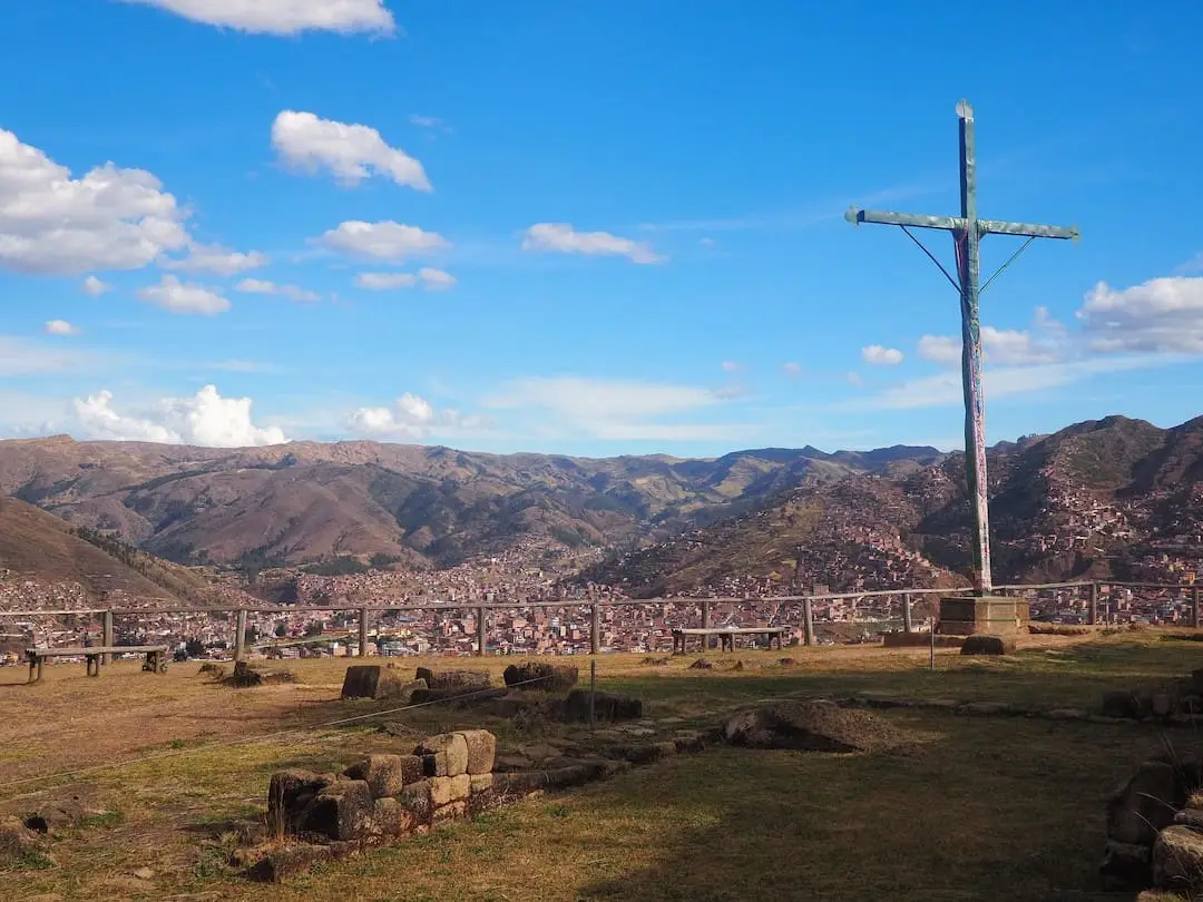 A wooden cross standing on a grassy area overlooking red roofed houses below