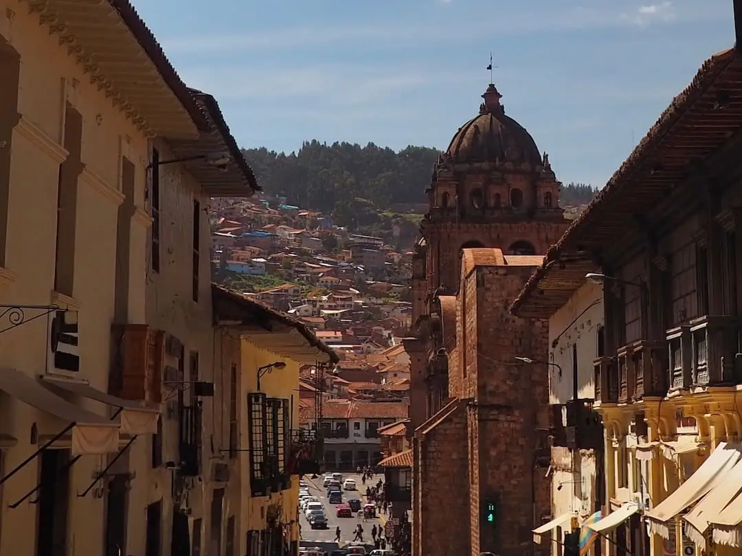 A narrow shopping street with a church on the right and red roofed houses in the background