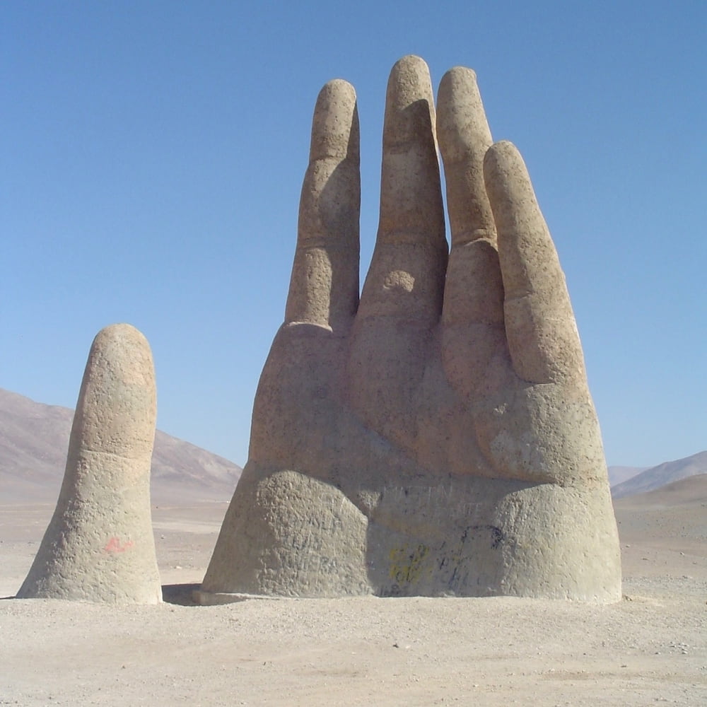 A large sculpture of a hand emerges from the desert sand