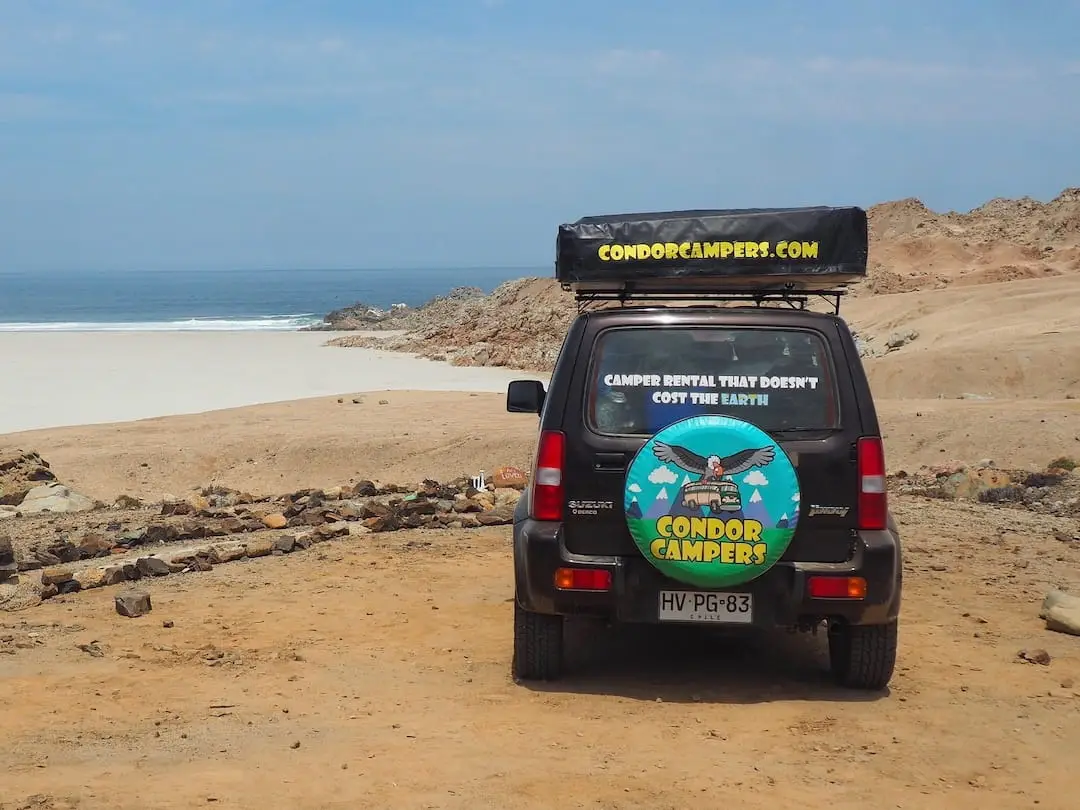 A jeep with rooftop tent parked overlooking a beach
