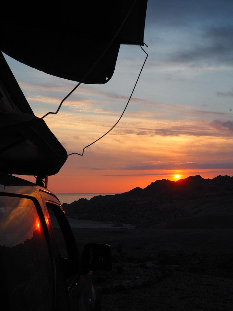 Side view of a car and rooftop tent in the foreground and a sunset in the background