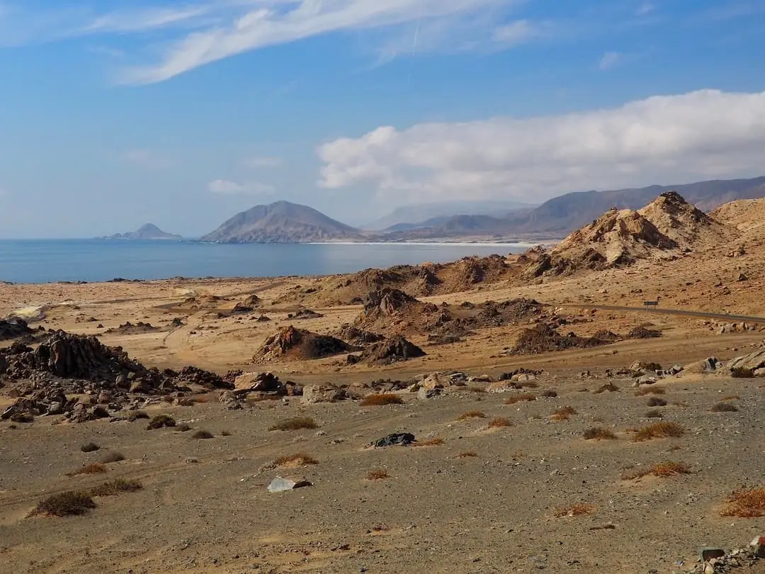 A desert road with sea and hills in the background
