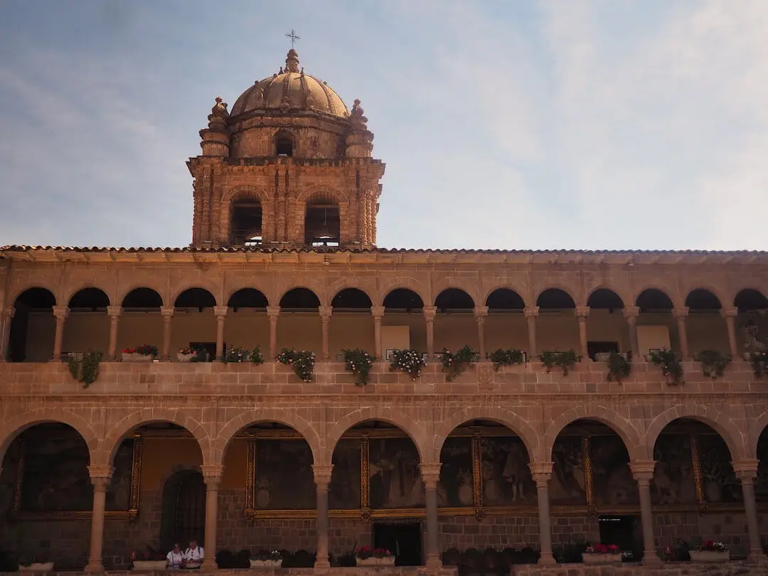 A brown building on two floors with large arches on the bottom floor and smaller arches on the upper and a dome behind