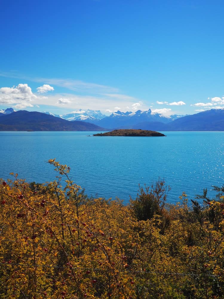 Lake in the foreground with a small island in the middle of it and snow-capped mountains in the background