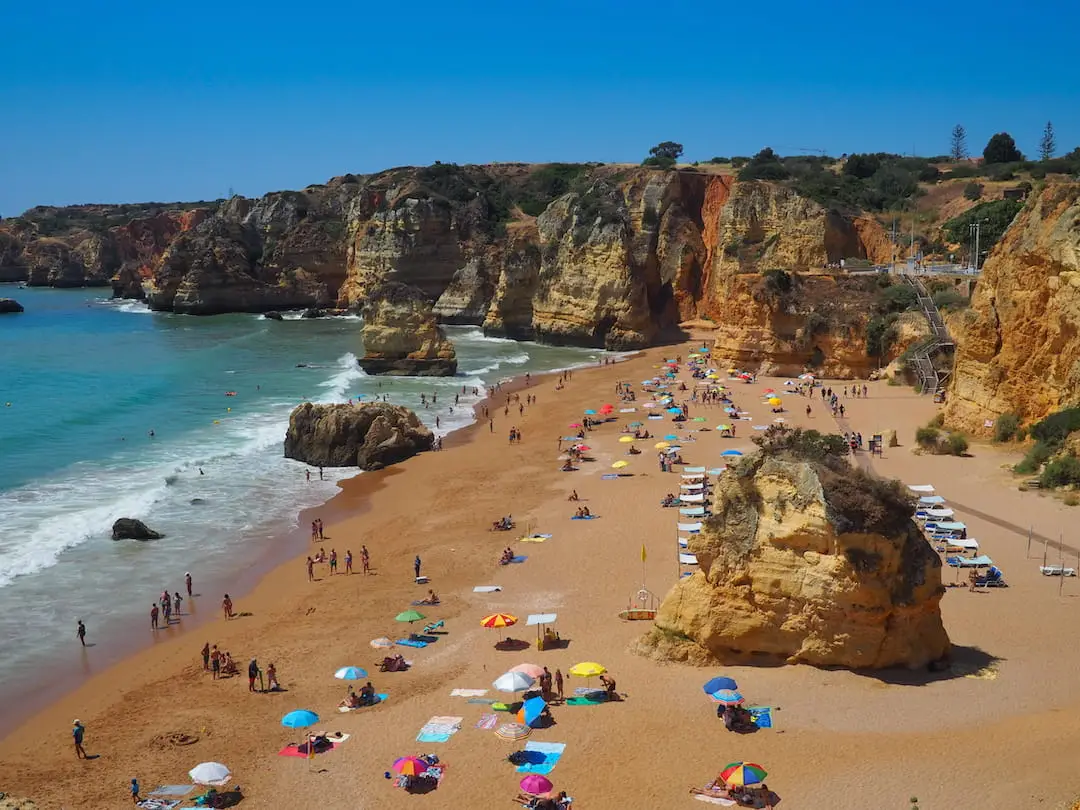 A golden beach backed by sandstone cliffs, with a large rock in the centre A red bicycle is parked outside a building with iron grills on the window
