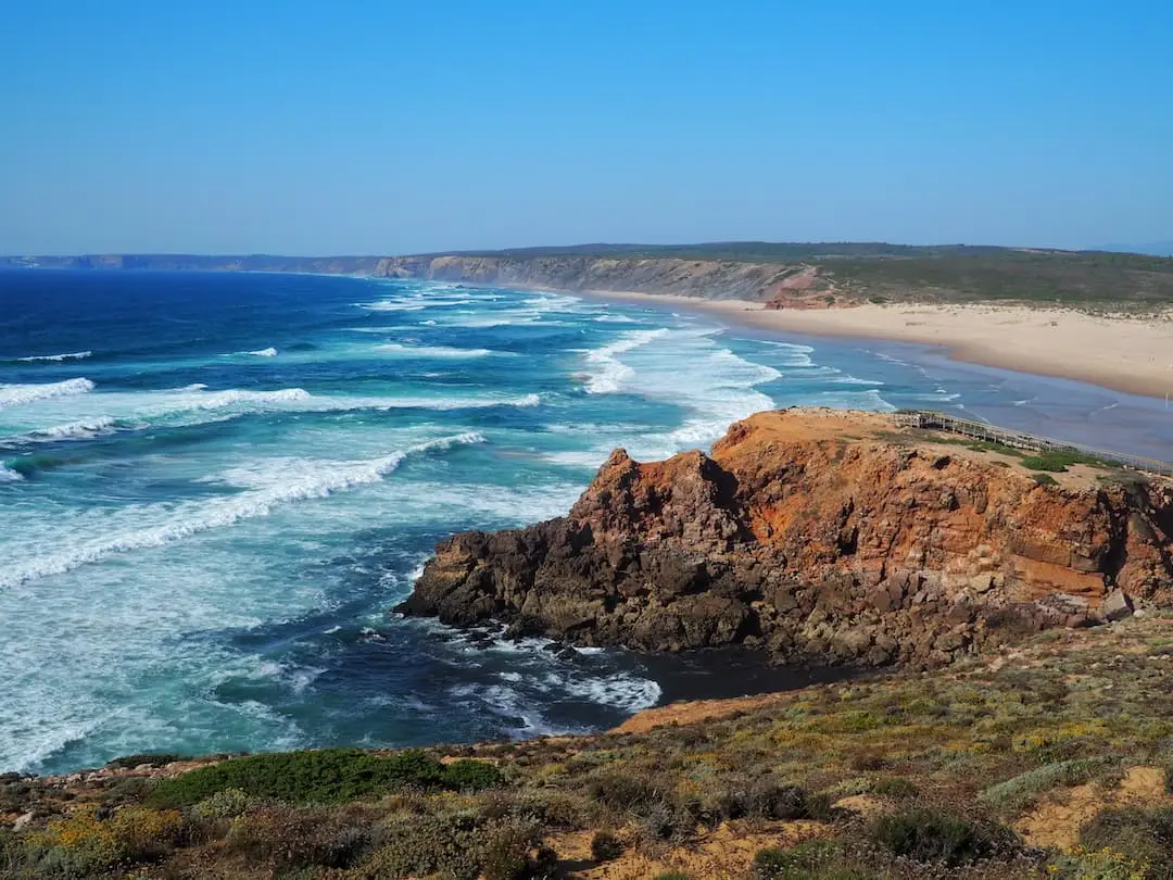 Praia da Bordeira, Carrapateira. A rocky outcrop in front of large waves crashing on to a sandy beach