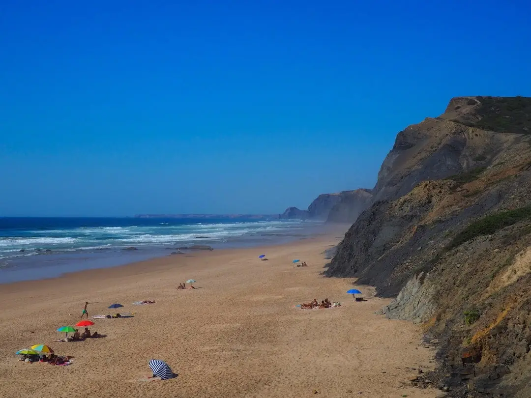 Praia da Cordoama, Vila do Bispo Sandy beach below cliffs with umbrellas and sunbathers