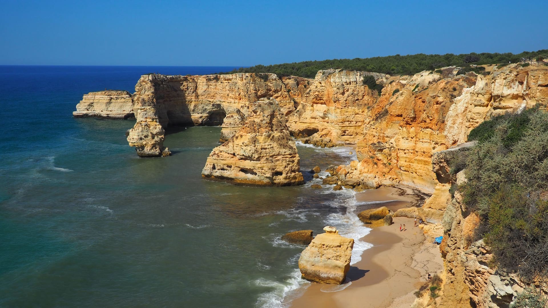 A golden sand beach surrounded by sandstone cliffs and large rocks just offshore