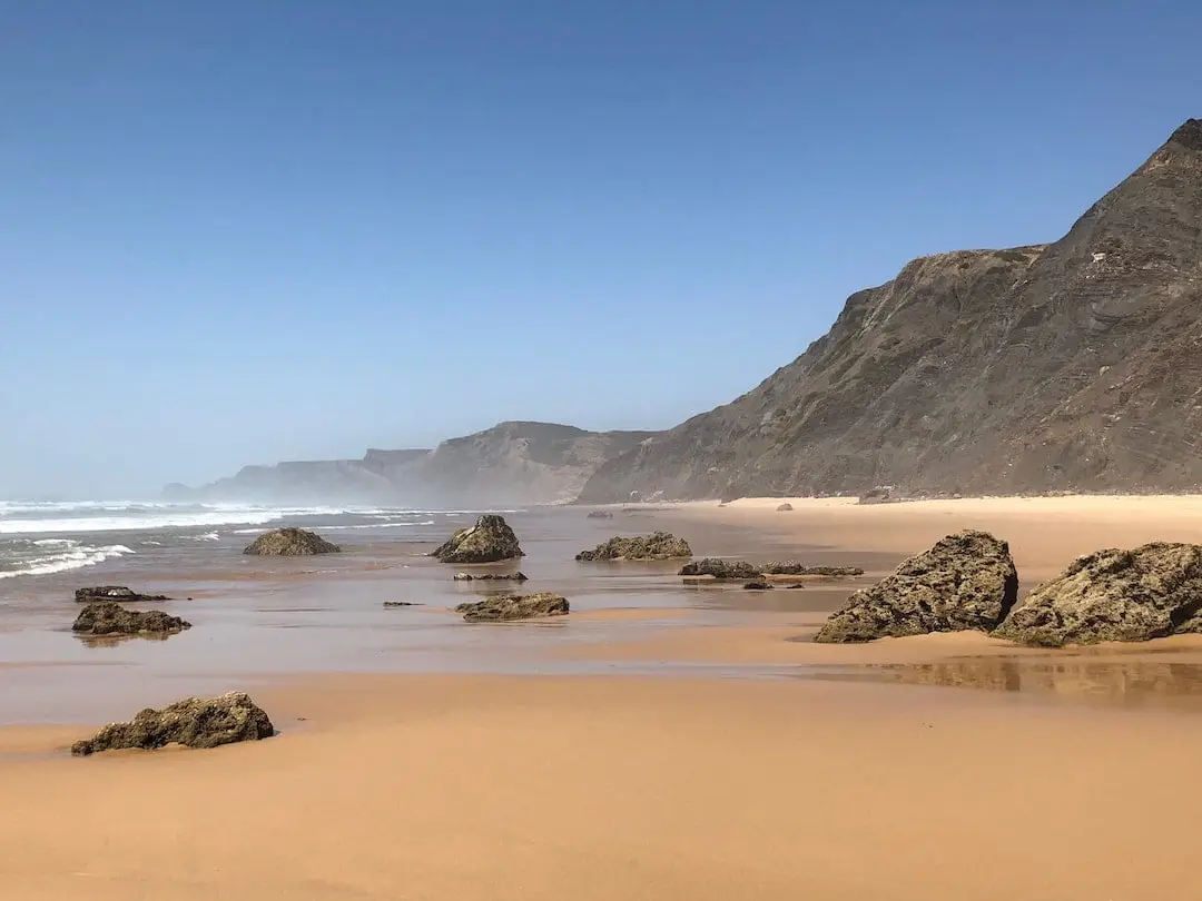Praia de Castelejo, Vila da Bispo. An empty beach with cliffs at the rear and rocks embedded in the sand