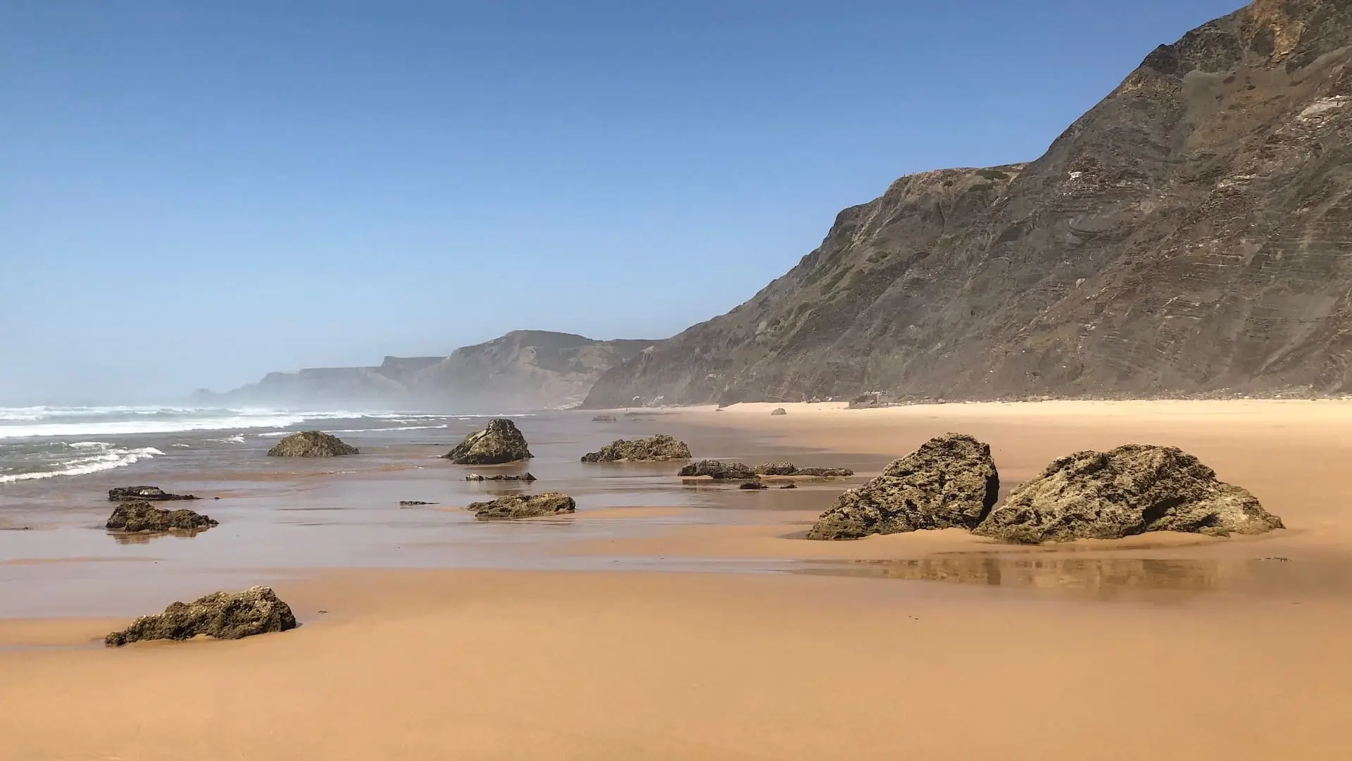Praia do Castelejo, Vila do Bispo An empty beach with cliffs at the rear and rocks embedded in the sand