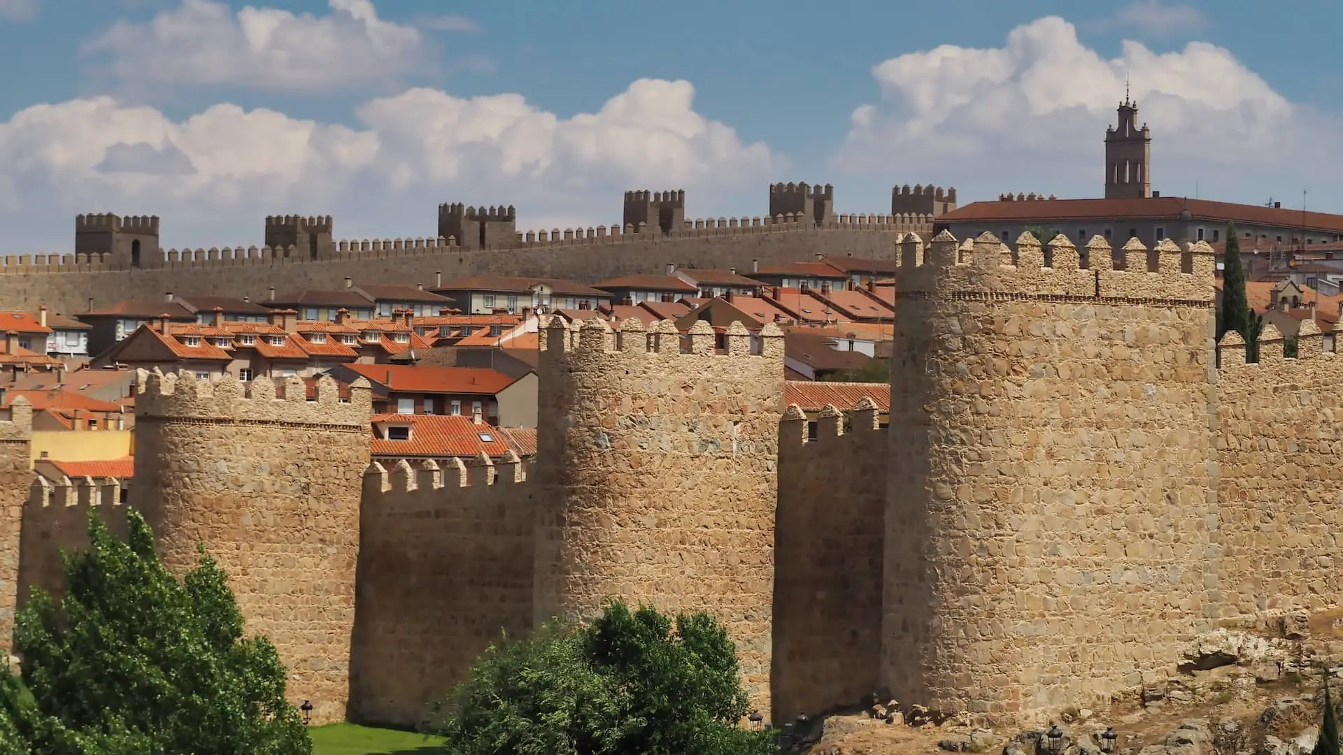 Day Trips from Madrid - Avila A wall with turrets surrounding red-roofed buildings