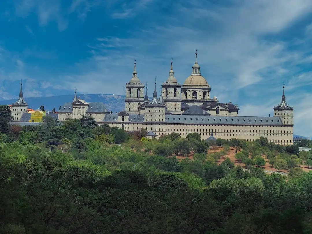 Day Trips from Madrid - El Escorial..... A palace with domed ceilings behind a forest of trees and blue skies behind
