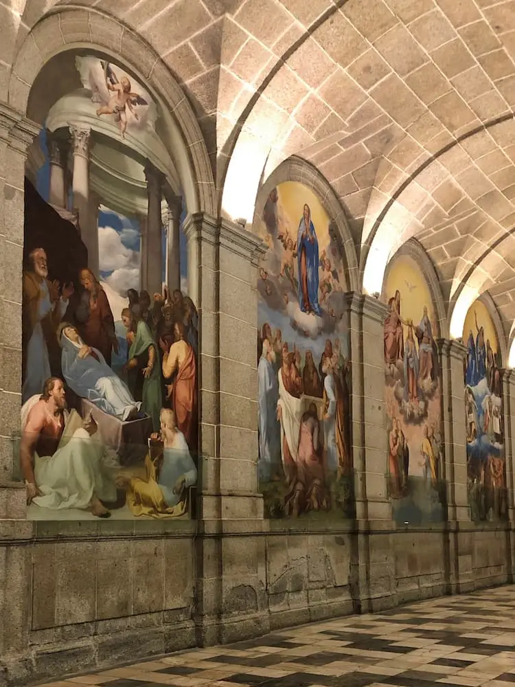 Day Trips from Madrid - El Escorial. 3 arches on a stone wall containing religious paintings