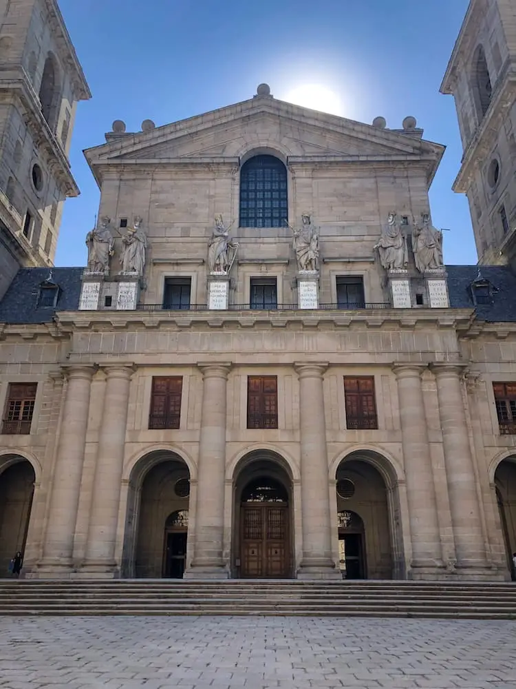 Day Trips from Madrid - El Escorial A building with three archways with a partly-hidden sun behind