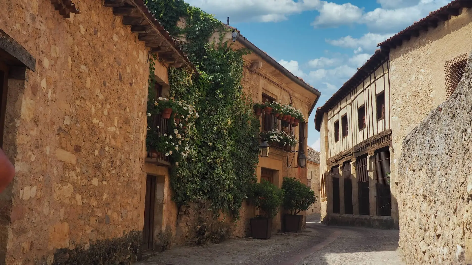 Day Trips from Madrid - Pedraza.. A medieval street with stone buildings covered in green foliage