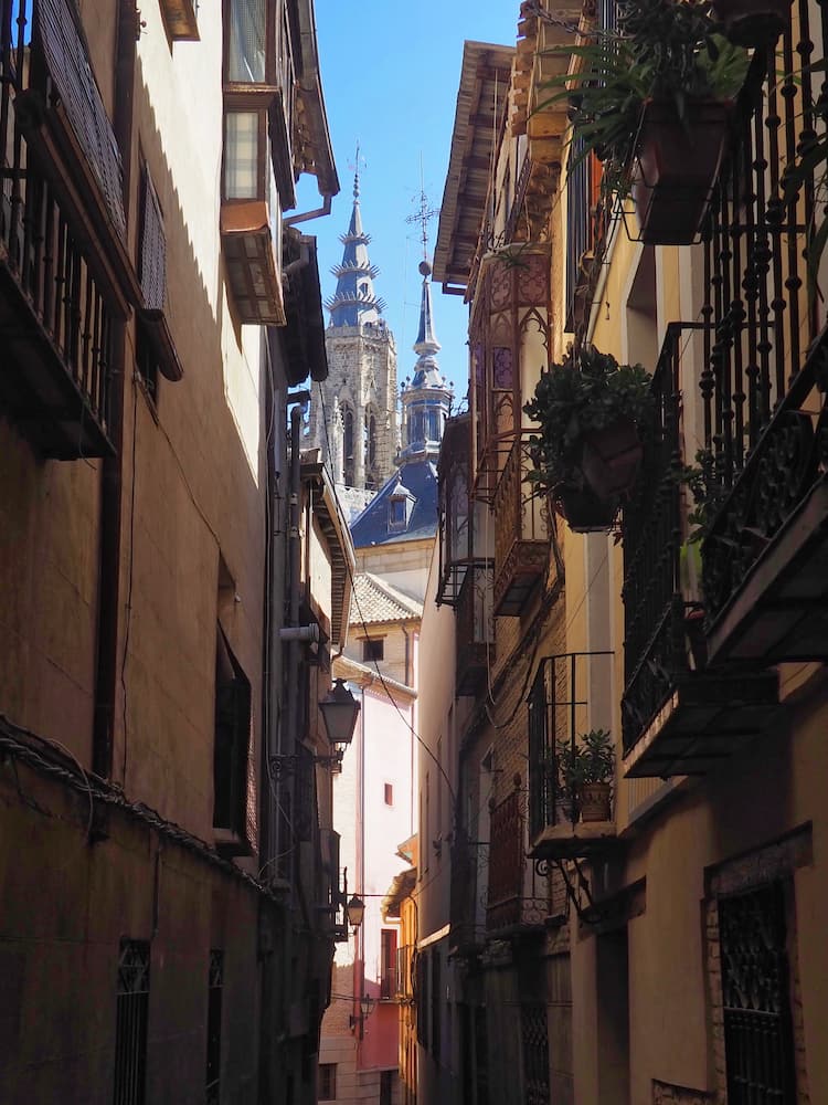 A narrow street with a cathedral spire in the background