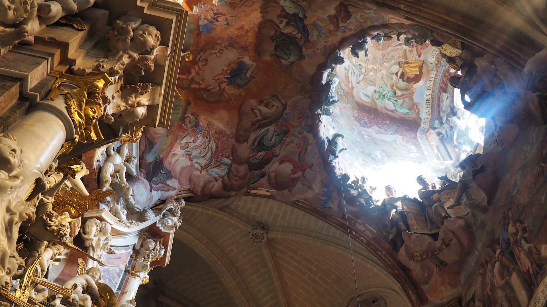A ceiling fresco painting is illuminated by light shining through a dome above