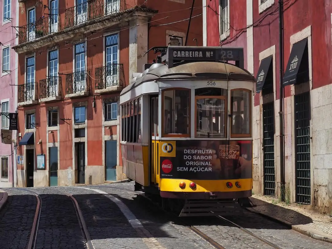 A yellow tram approaches within a street of red buildings