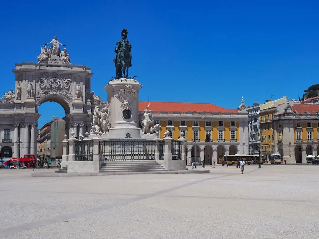 A statue of a man on a horse stands in front of an archway and a row of yellow buildings with red rooftops