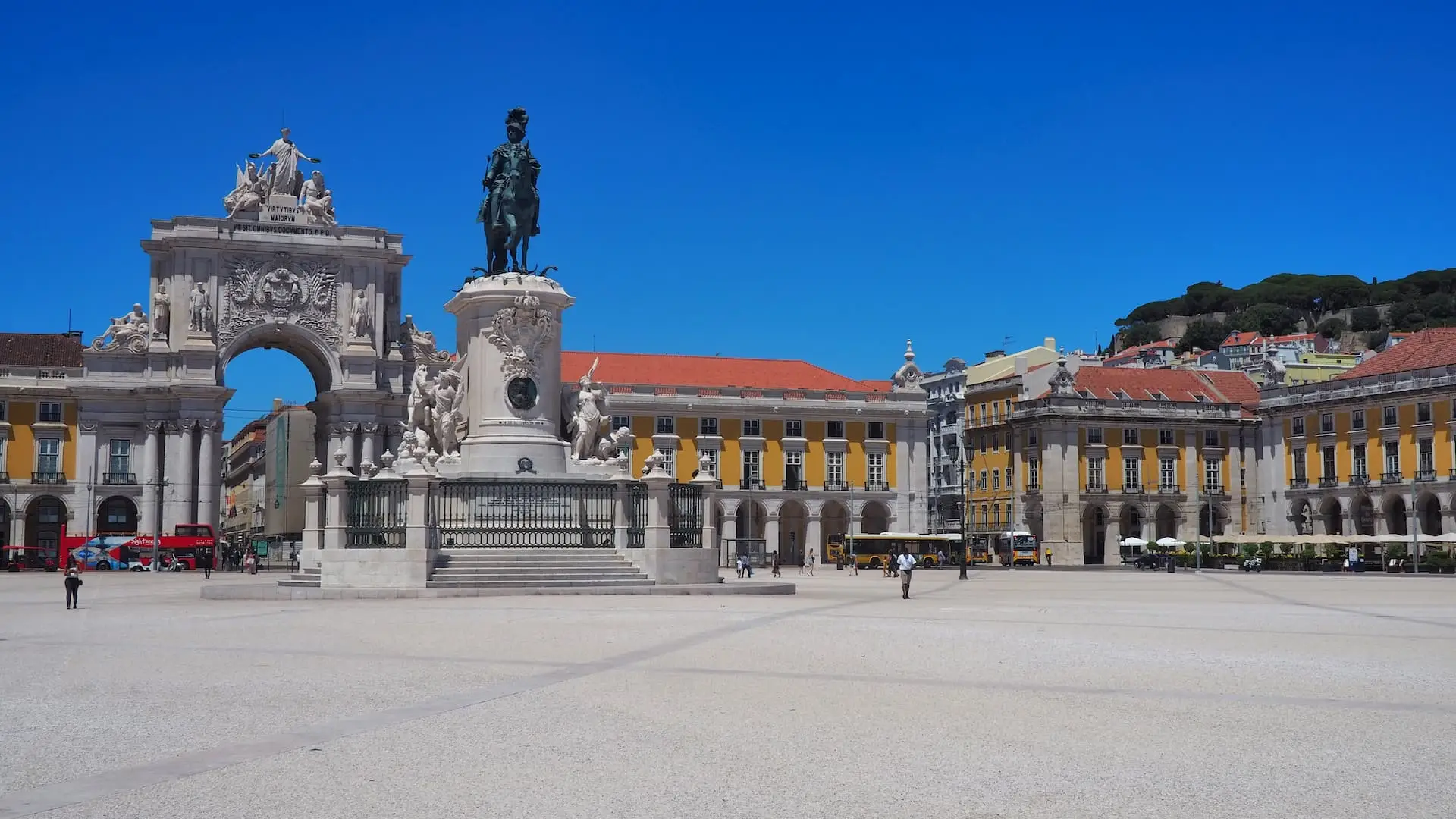 A statue of a man on a horse stands in front of an archway and a row of yellow buildings with red rooftops