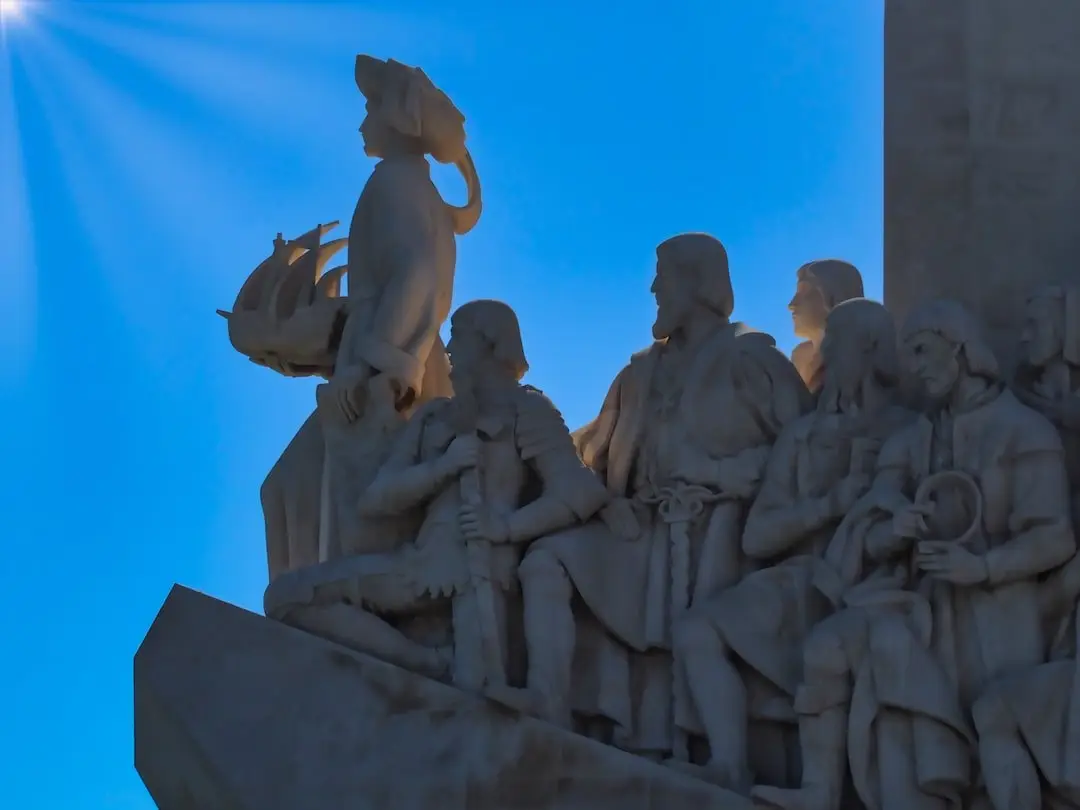 A collection of statues look out towards the sea while the sun reflects on one side