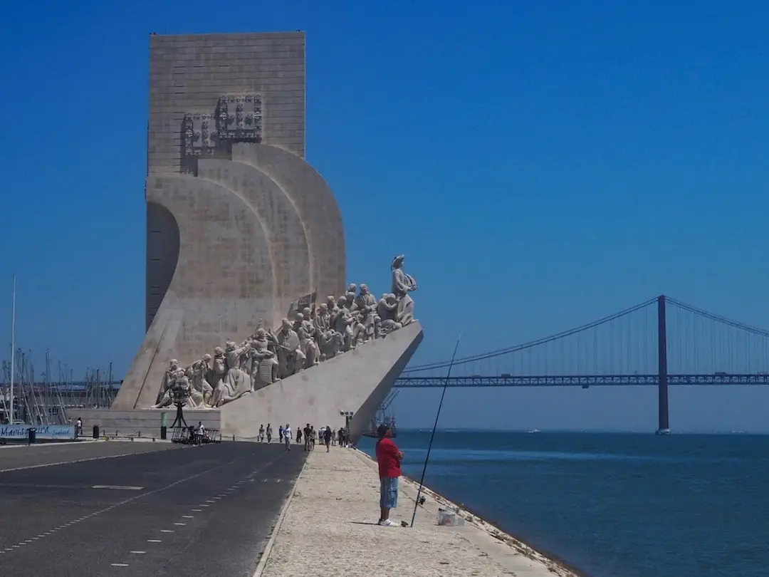 A stone sculptured monolithic structure stands beside the sea with a man and his fishing rod in the foreground f