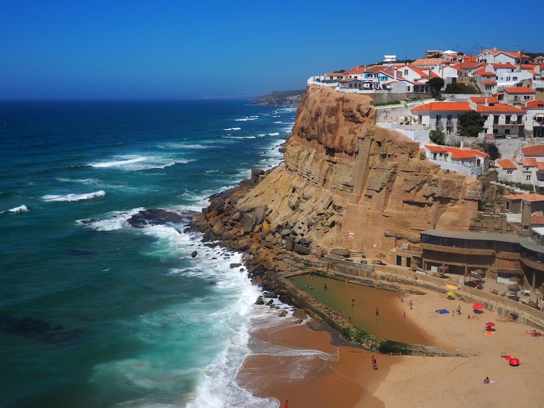 A golden beach sits below a cliff-top village of white houses and red roofs
