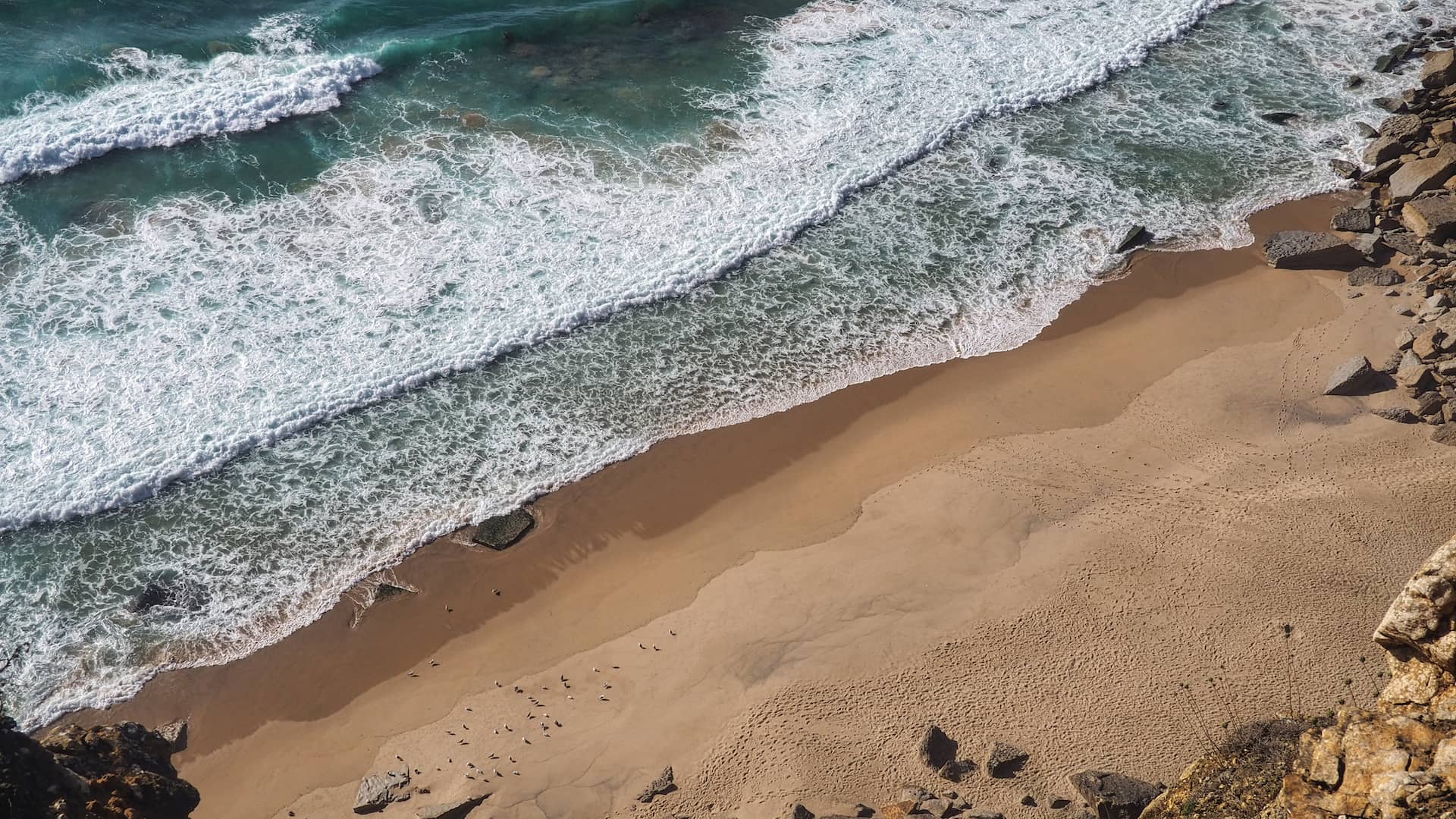 Aerial view of waves crashing on to a golden beach