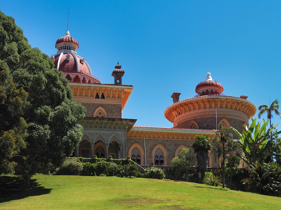 A garden leads to a brightly coloured palace with orange walls and a pink dome