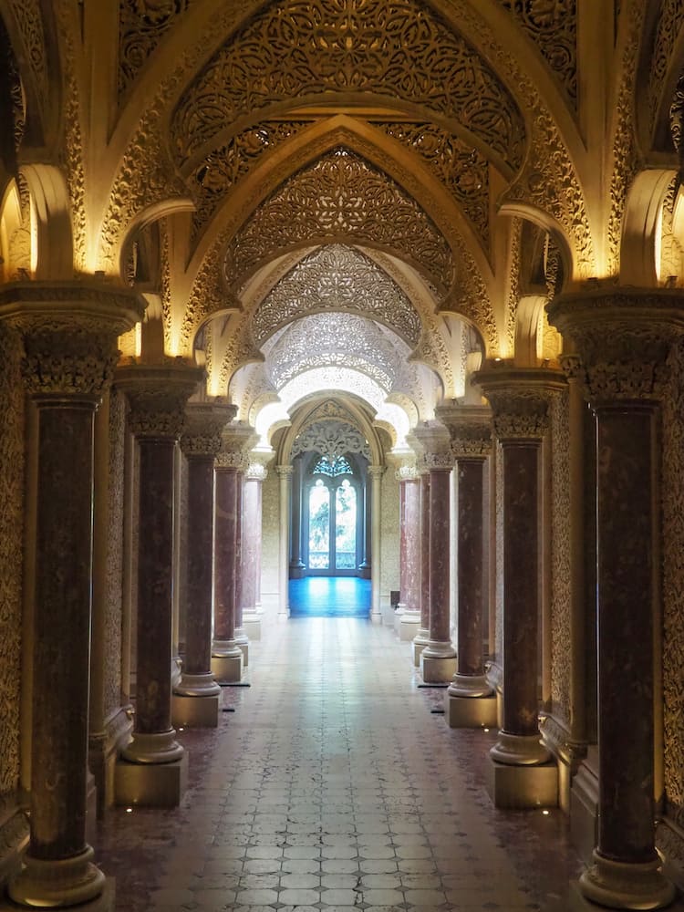 A hallway with a golden arched ceiling and marble pillars either side