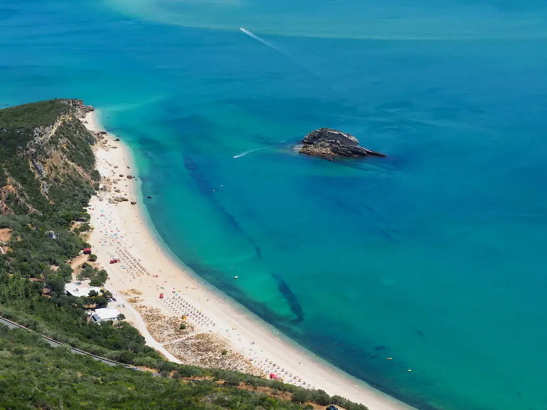 Forested cliffs leading down to a white beach and turquoise/blue sea