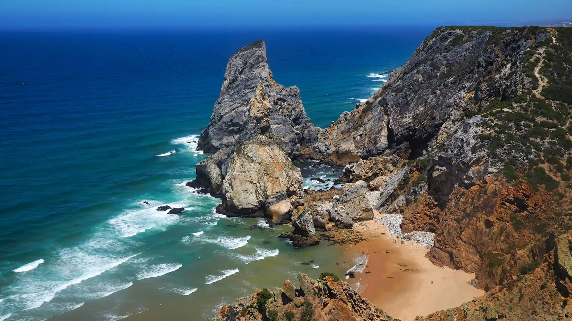 A golden beach separates rocky cliffs with a turquoise/blue sea