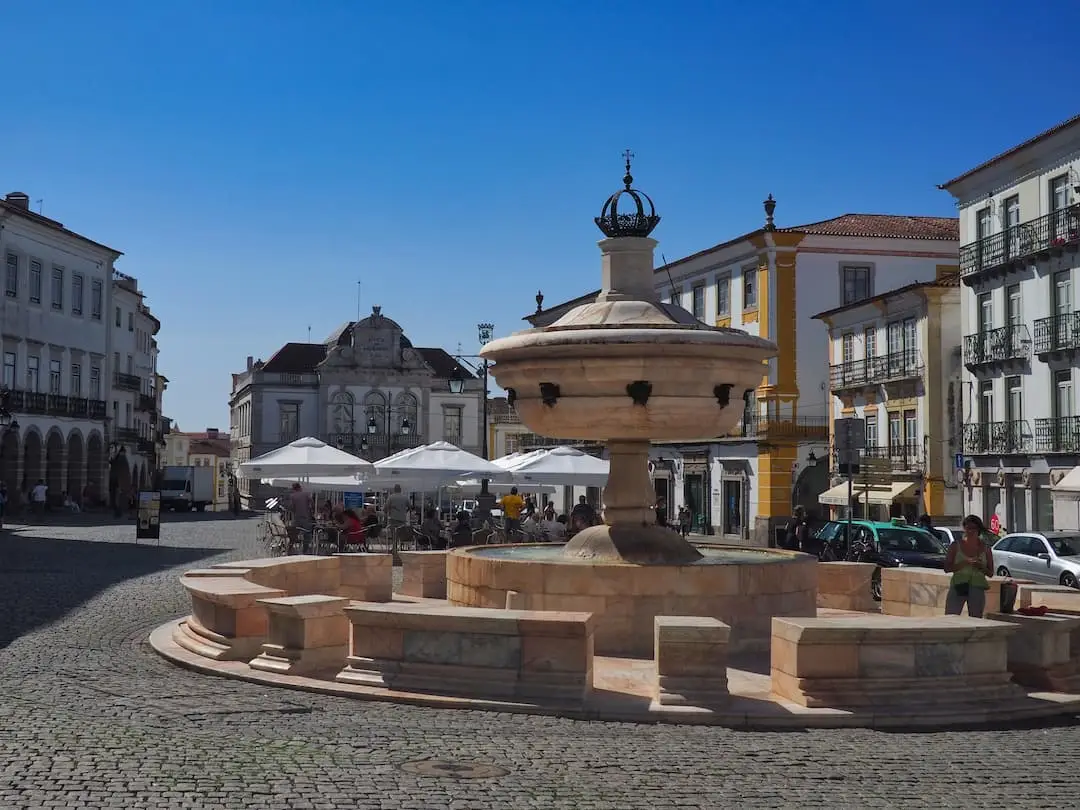 A circular stone fountain in the foreground and buildings in the background