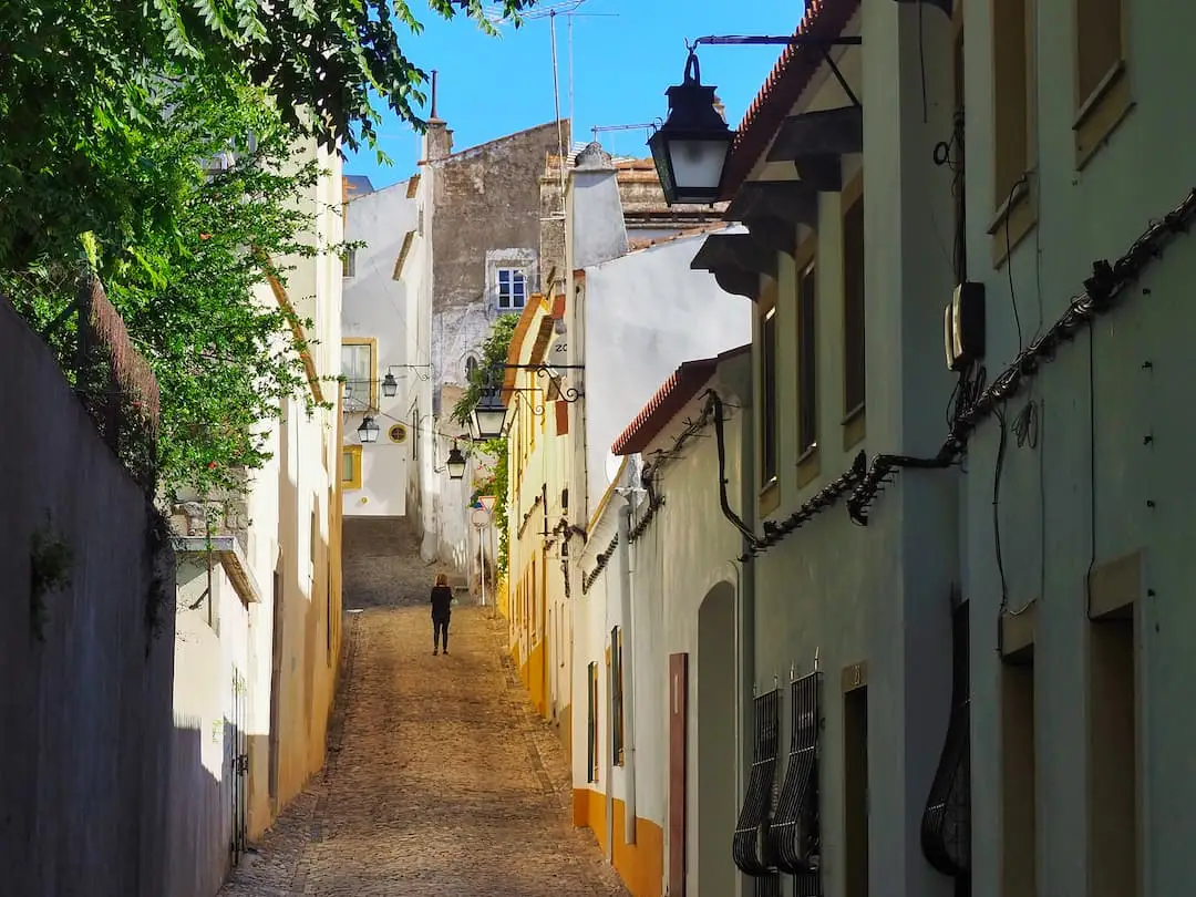 A woman stands in an otherwise empty cobblestoned street