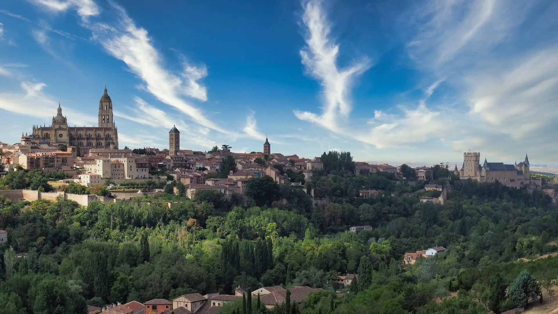 Segovia - the cathedral and castle A town with a cathedral on the left, castle on the right and trees in the foreground