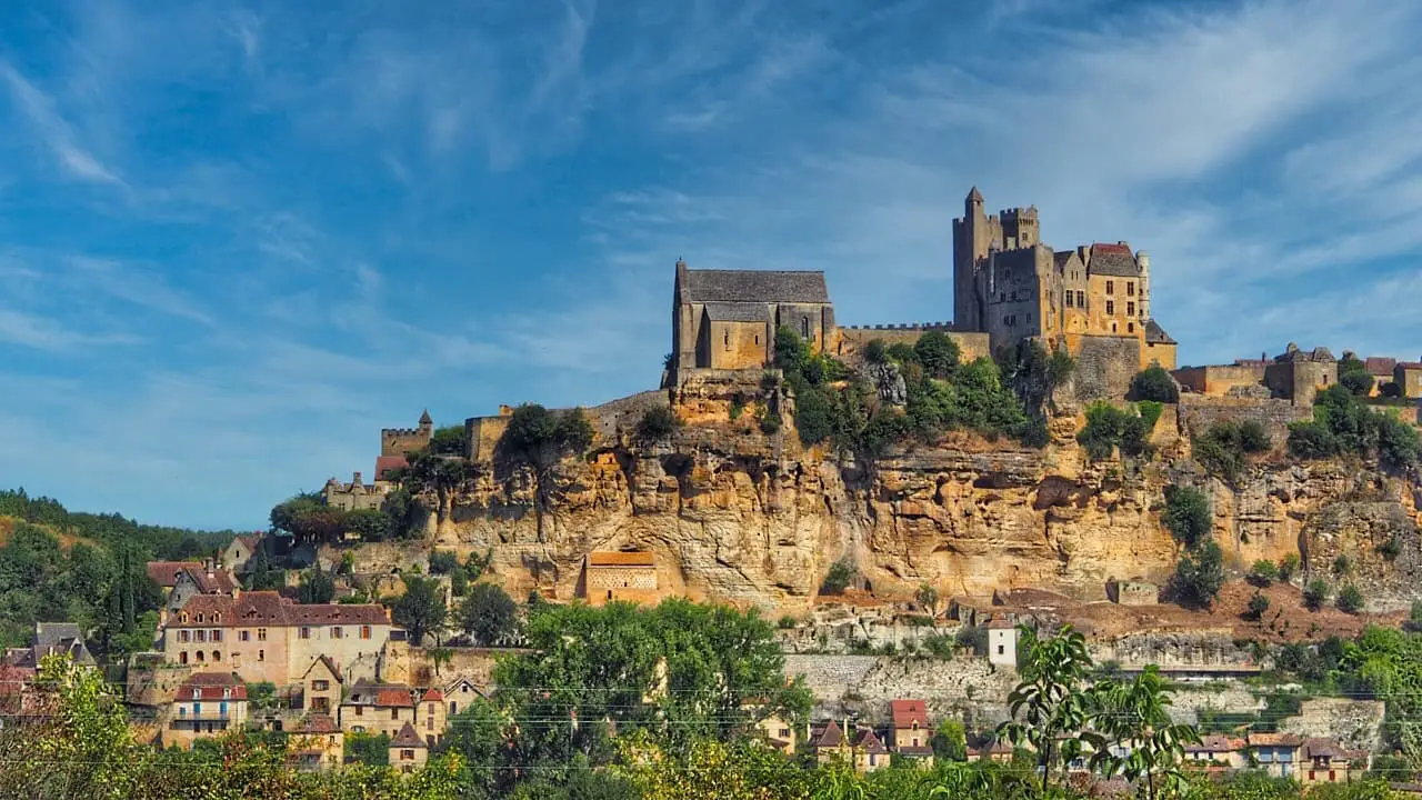 A sandstone castle sits on top of a rock with a village below