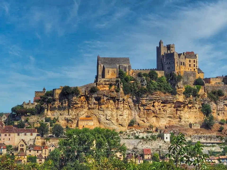 A large building with turrets looks our over a river with cliffs to the side